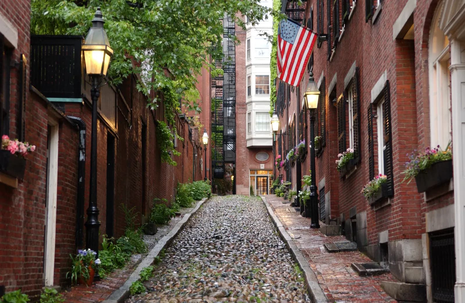 Acorn Street in Beacon Hill, Boston: a narrow cobblestone lane between brick row houses with gas lamps and window boxes