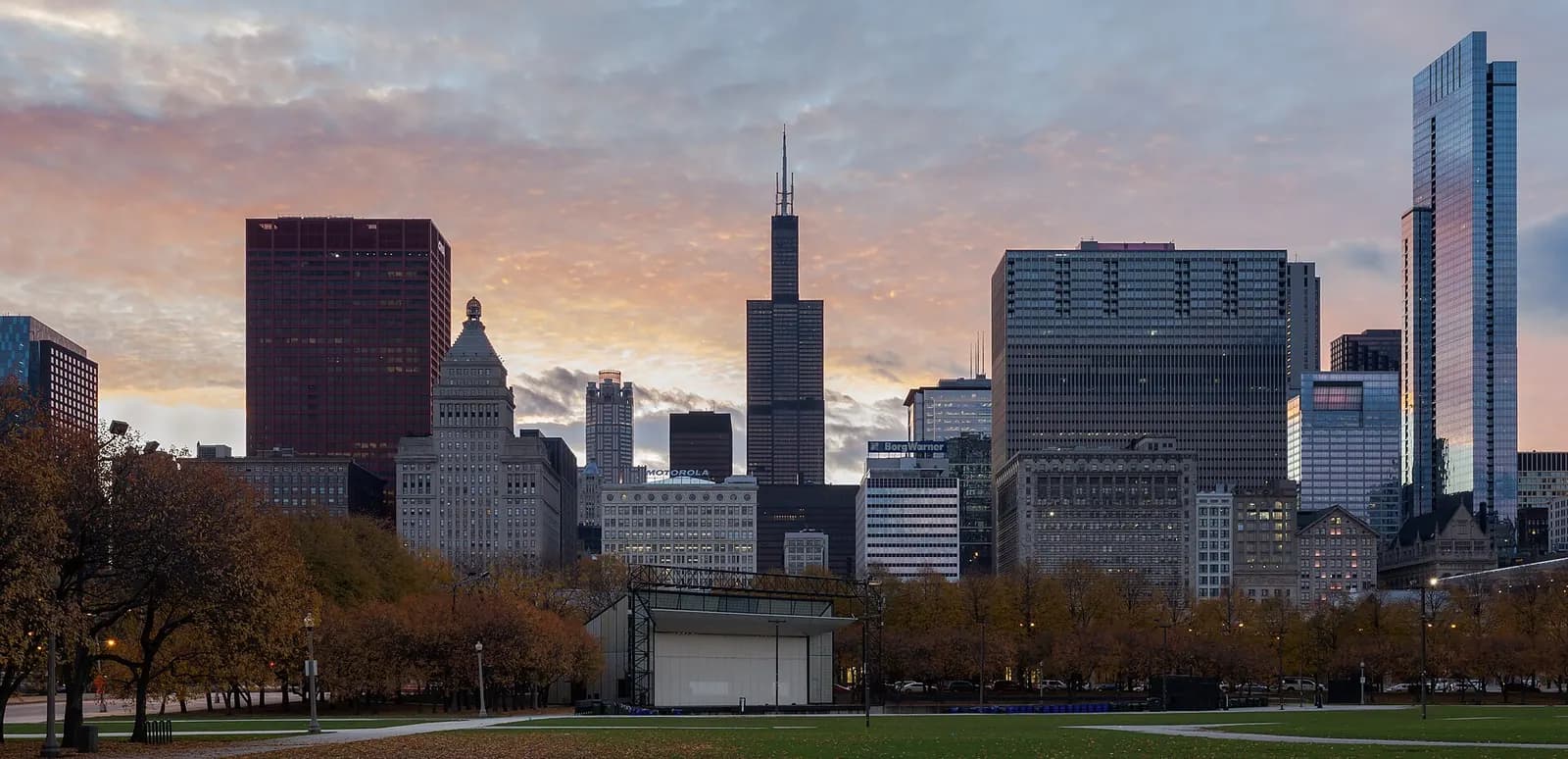 The Chicago skyline at sunrise seen across Grant Park, with the Willis Tower above autumn trees